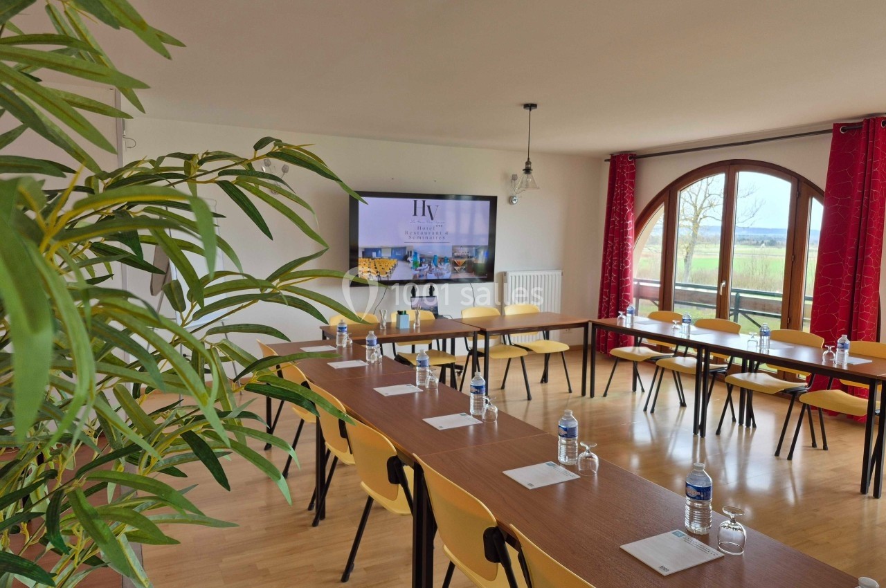 Salle de réunion lumineuse avec tables disposées en U, chaises jaunes, écran, et vue sur l'extérieur par une grande baie…