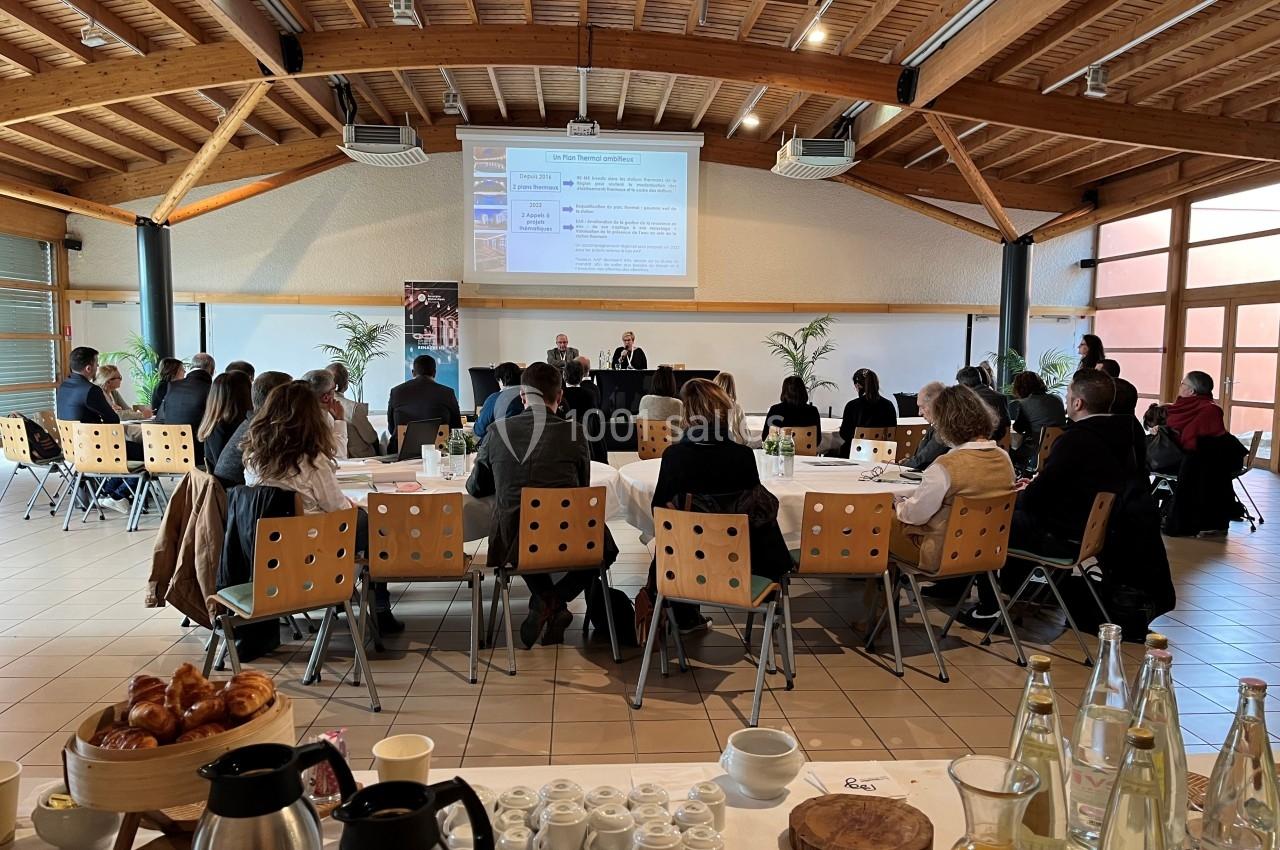 Participants assis dans une salle de conférence lumineuse, écoutant une présentation projetée sur un écran.