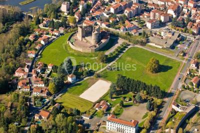 Vue aérienne d'un château médiéval entouré de verdure, au cœur d'une petite ville avec des habitations et des routes.