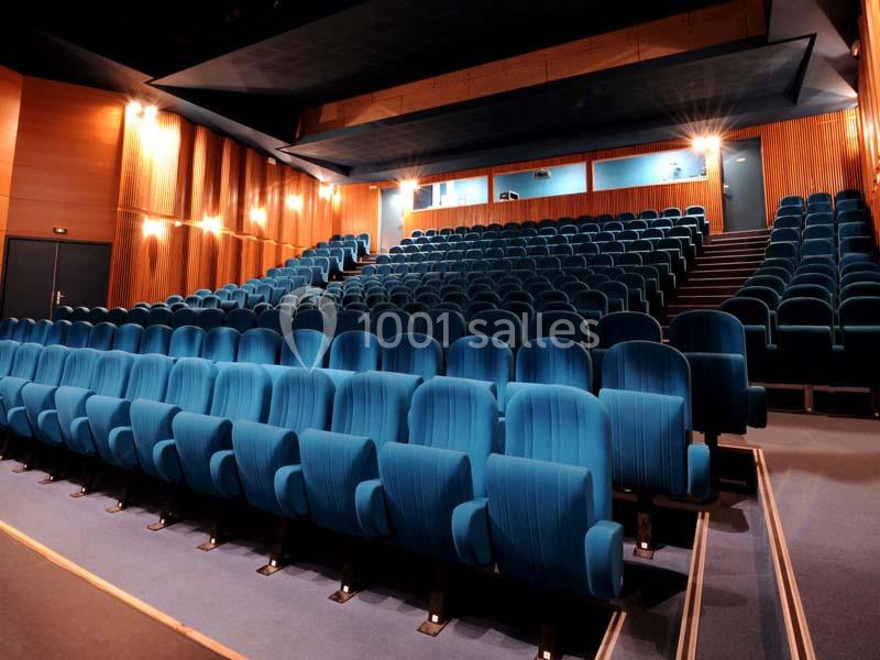 Salle de cinéma vide avec des rangées de fauteuils bleus et des murs en bois éclairés par des appliques murales.