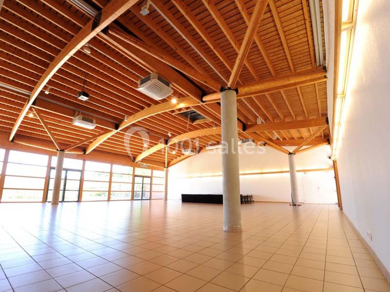 Salle spacieuse avec plafond en bois, grandes baies vitrées, carrelage clair et éclairage intégré.