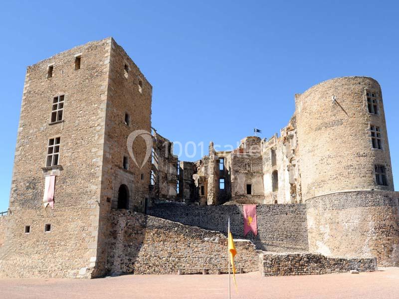 Ruines d'un château médiéval avec tours en pierre, drapeaux colorés et ciel bleu en arrière-plan.