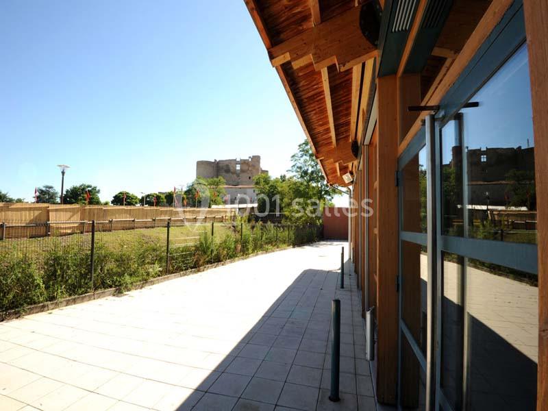 Terrasse pavée bordée d'un bâtiment en bois avec vue sur un château en arrière-plan sous un ciel dégagé.