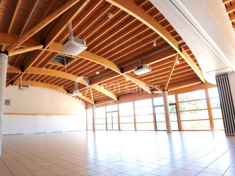 Grande salle lumineuse avec plafond en bois, larges fenêtres et carrelage clair, adaptée à des événements ou réunions.