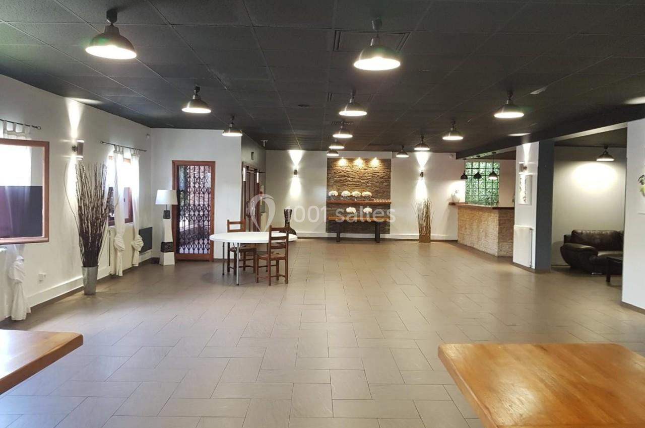 Salle spacieuse avec sol en carrelage, plafond noir, tables en bois, éclairage suspendu et décoration sobre.