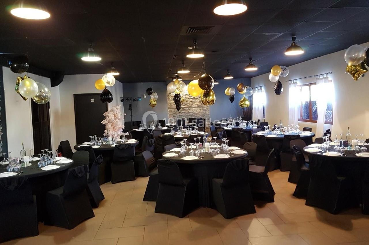 Salle de réception décorée avec des ballons noirs, dorés et blancs, tables dressées avec nappes noires et vaisselle.