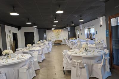 Salle spacieuse avec carrelage au sol, murs clairs, plafond noir, tables et chaises dispersées.