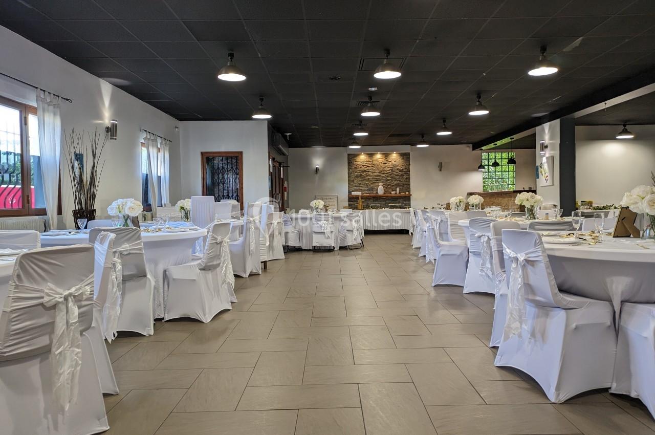 Salle de réception élégamment décorée avec des tables rondes, nappes blanches et chaises couvertes de housses.