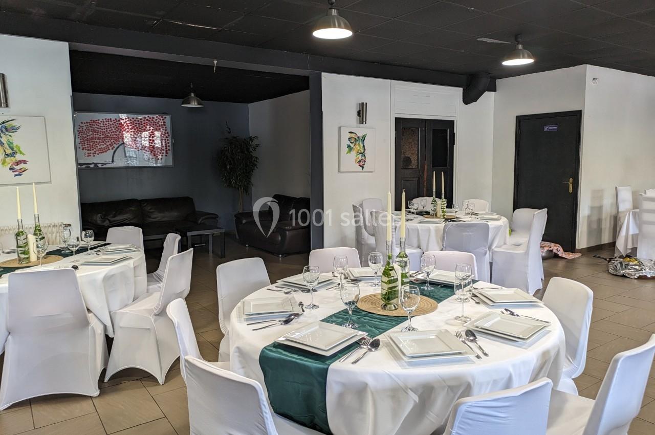 Salle de réception avec tables rondes dressées, nappes blanches, chemins de table verts et chaises houssées.