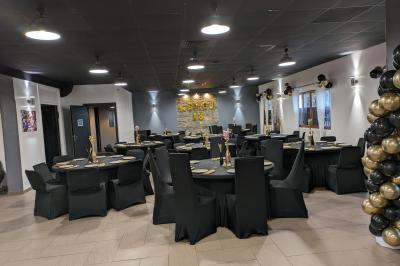 Salle spacieuse avec carrelage au sol, murs clairs, plafond noir, tables et chaises dispersées.