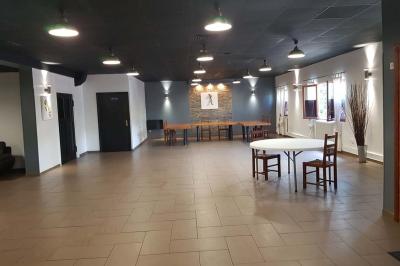 Salle spacieuse avec carrelage au sol, murs clairs, plafond noir, tables et chaises dispersées.