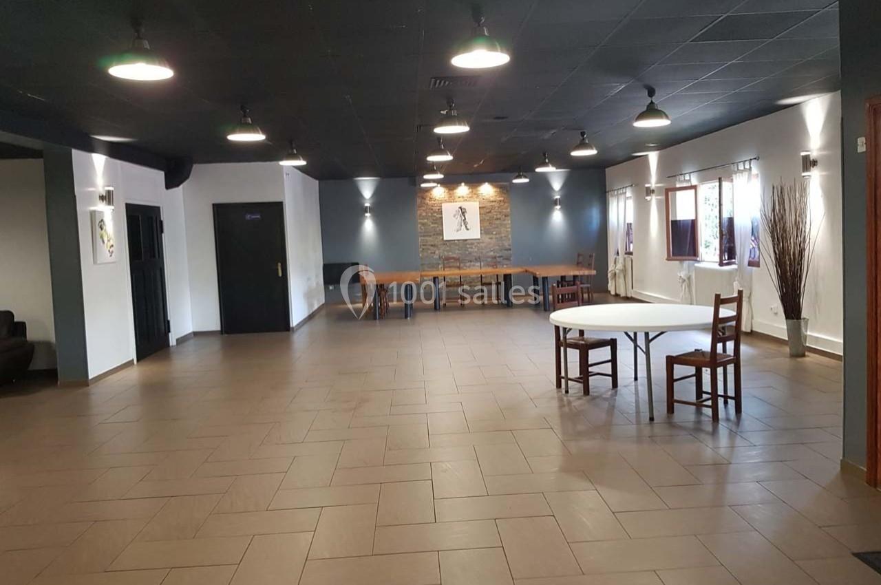 Salle spacieuse avec carrelage au sol, murs clairs, plafond noir, tables et chaises dispersées.