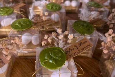 Petits coffrets transparents contenant des dragées, décorés de cachets de cire verte et de fleurs séchées.