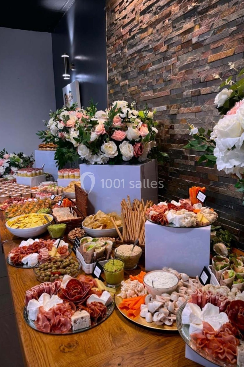 Buffet garni de charcuteries, fromages, légumes et pains, disposé sur une table en bois avec décor floral en arrière-plan.