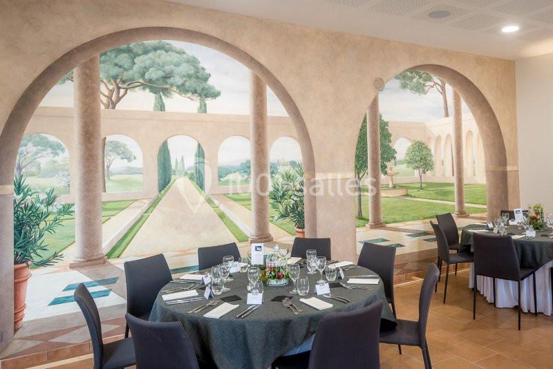 Salle de réception avec tables dressées, décorée d'une fresque murale représentant un jardin méditerranéen.