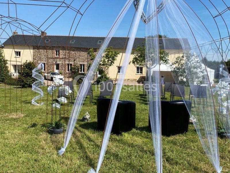 Structure métallique décorée de voiles blancs dans un jardin, entourée de chaises et de végétation.