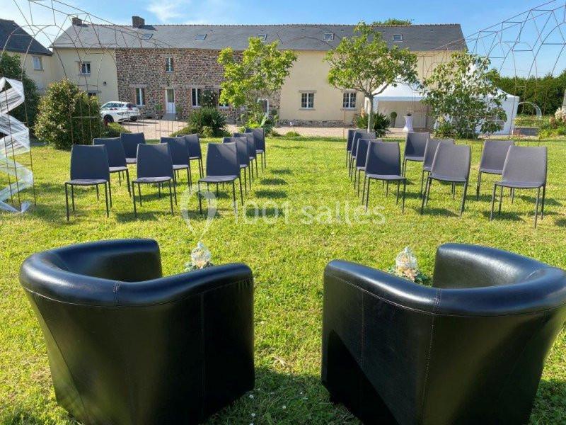 Chaises disposées en extérieur sur une pelouse, face à deux fauteuils noirs, avec des bâtiments en arrière-plan.