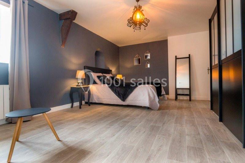 Chambre moderne avec mur bleu, lit double, parquet clair, miroir sur pied et éclairage suspendu.
