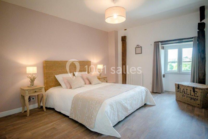 Chambre lumineuse avec lit double, murs pastel, parquet, deux tables de chevet et une fenêtre donnant sur l'extérieur.