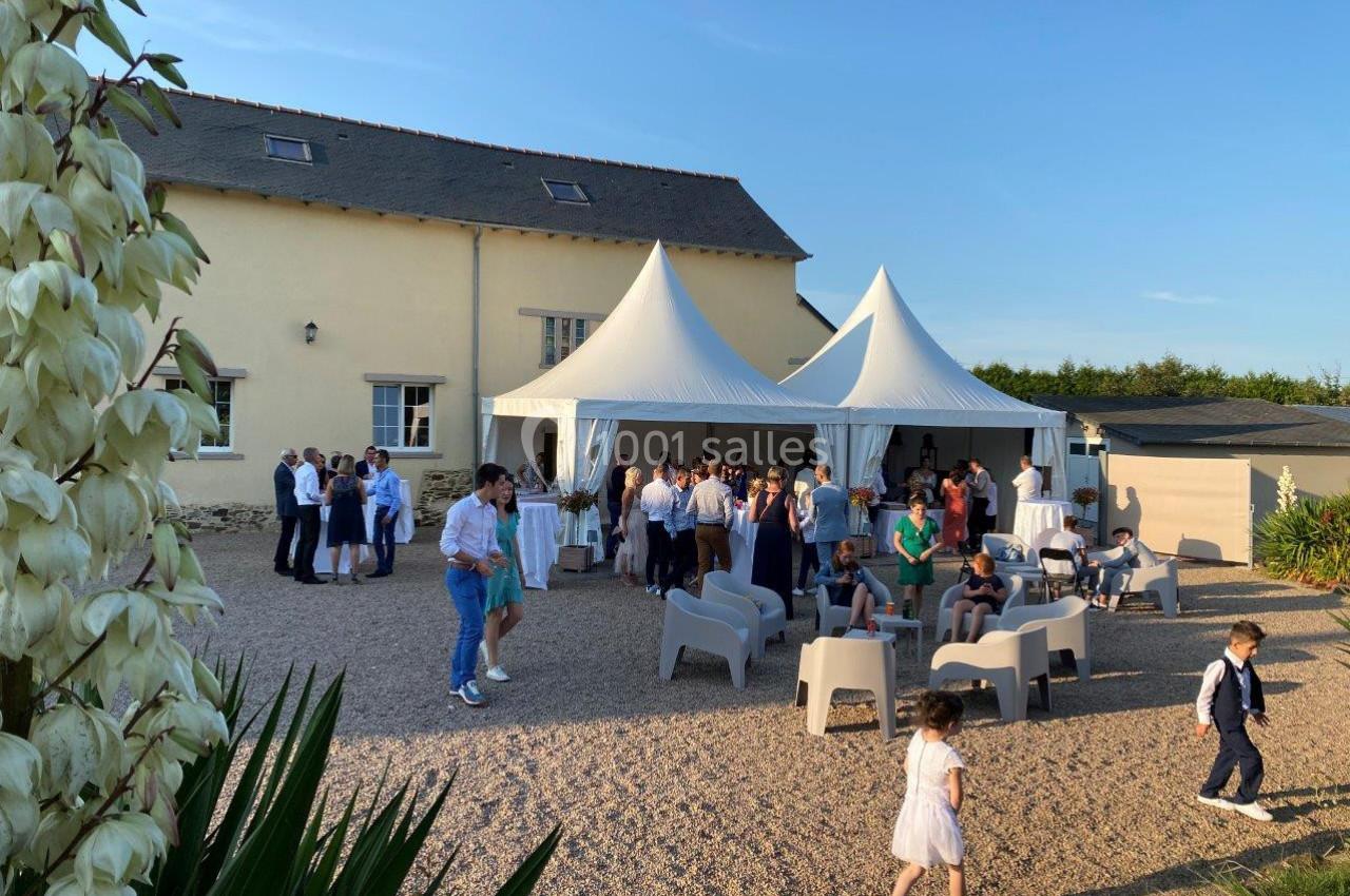 Groupe de personnes rassemblées dans une cour ensoleillée avec des tentes blanches et des chaises disposées.