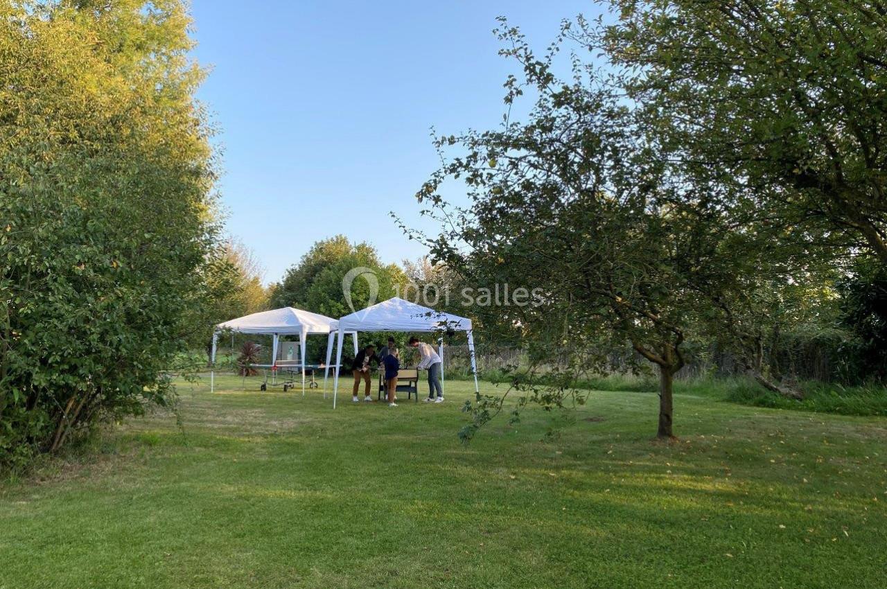 Deux tentes blanches installées dans un jardin verdoyant, avec quelques personnes debout à proximité.