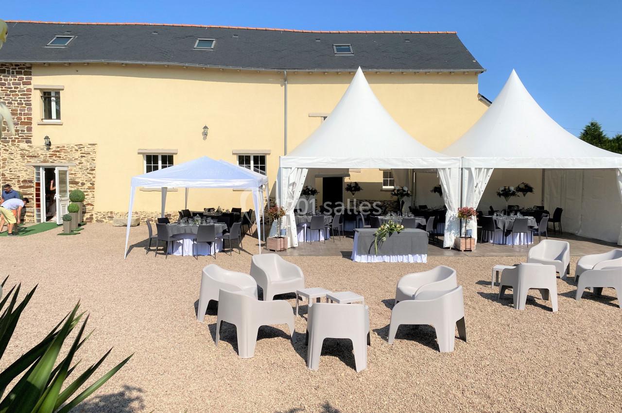 Espace extérieur avec barnums et chaises installés devant un bâtiment en pierre pour un événement en plein air.
