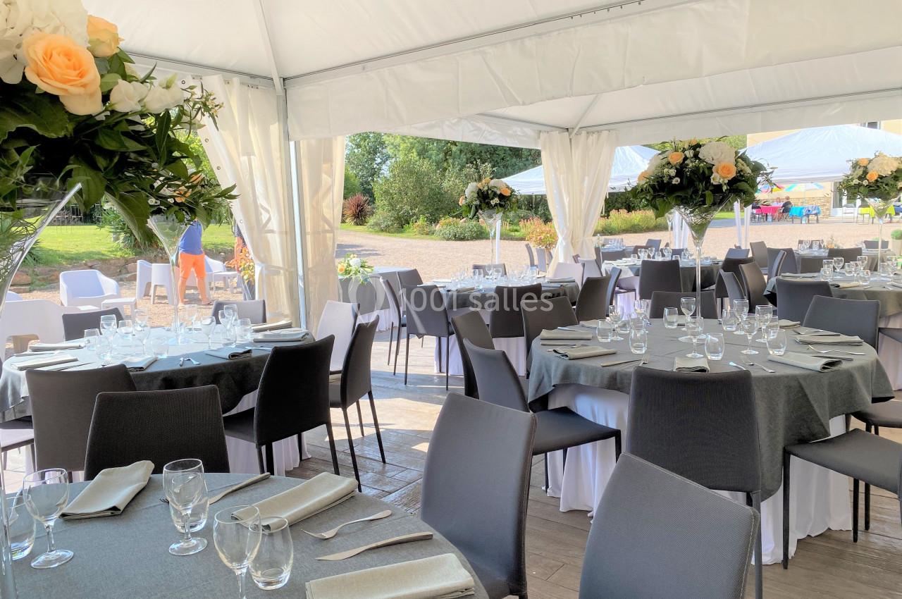 Salle de réception décorée avec des tables rondes, nappes grises, chaises noires et arrangements floraux.