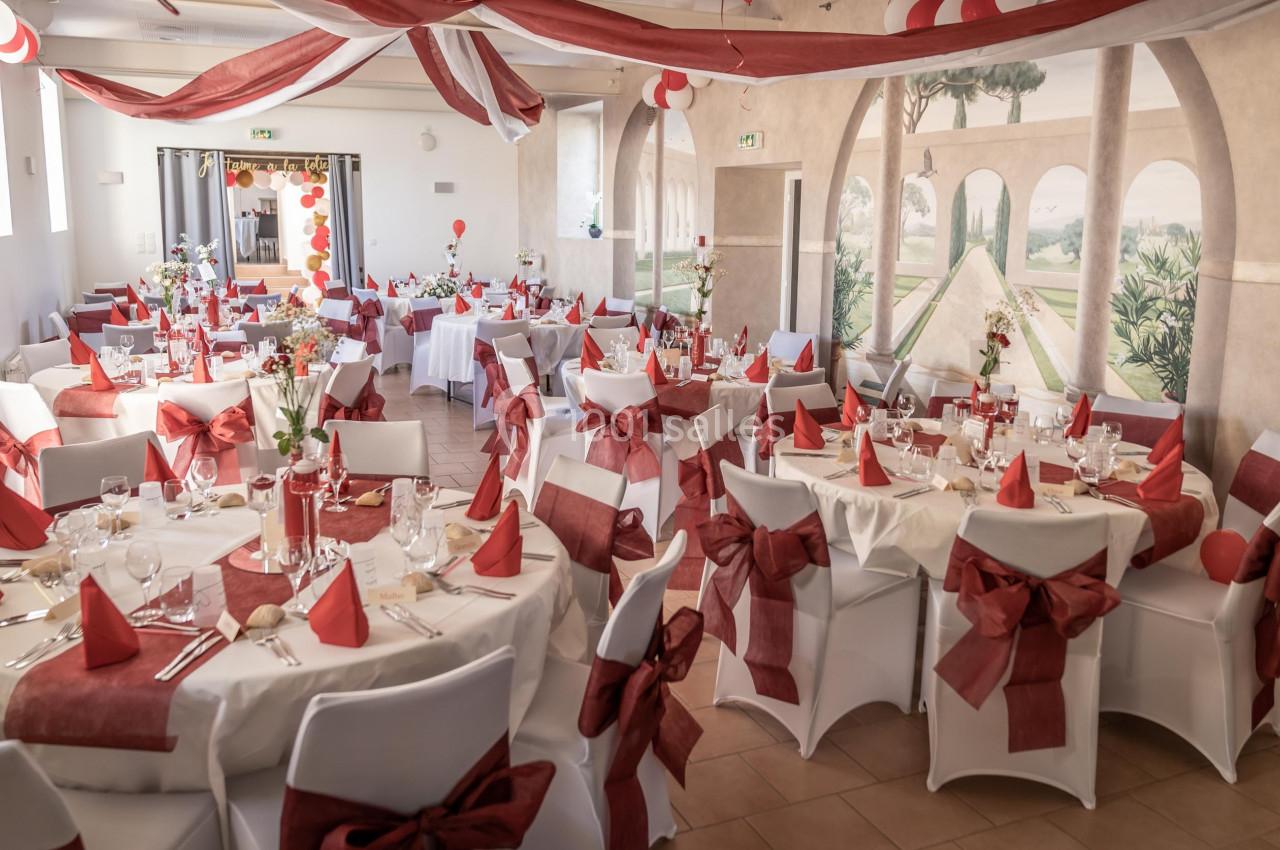 Salle de réception décorée avec des nappes blanches, des nœuds rouges sur les chaises et des tables dressées pour un…