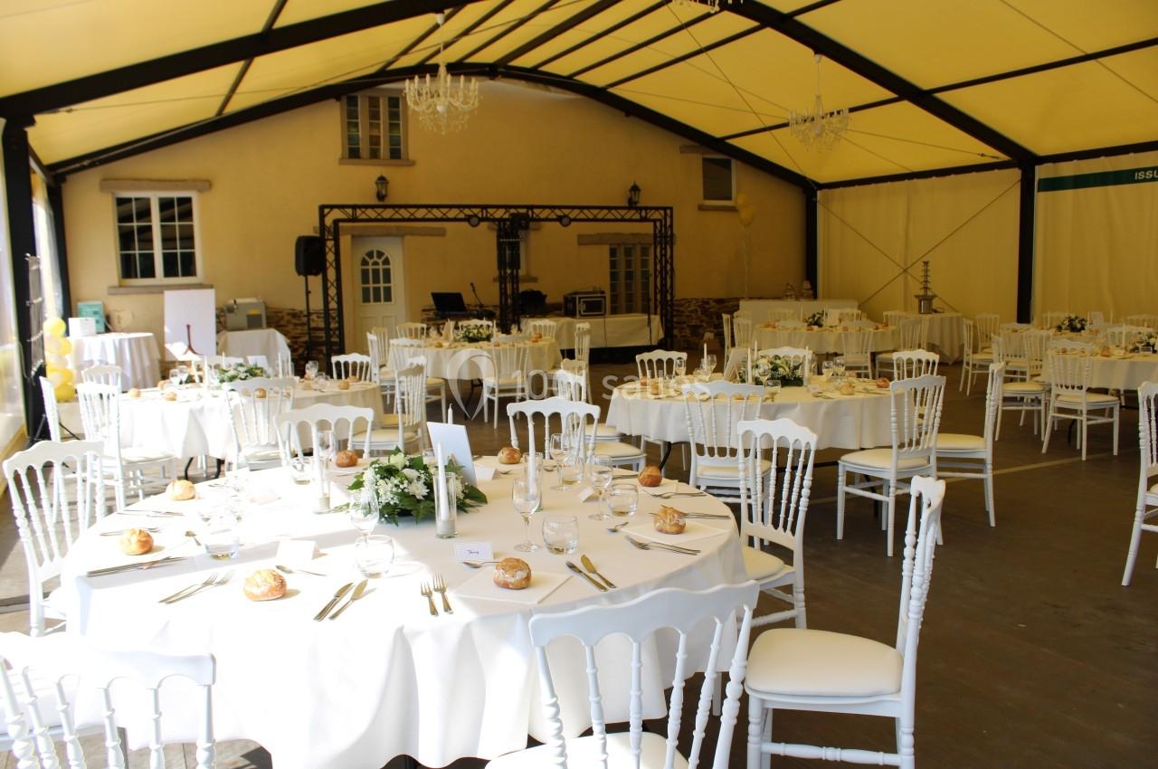 Salle de réception sous une tente avec tables rondes dressées, nappes blanches, chaises assorties et décorations florales.