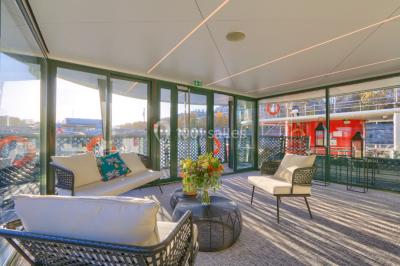 Espace intérieur lumineux avec baies vitrées donnant sur un quai, aménagé avec des fauteuils et une table basse.