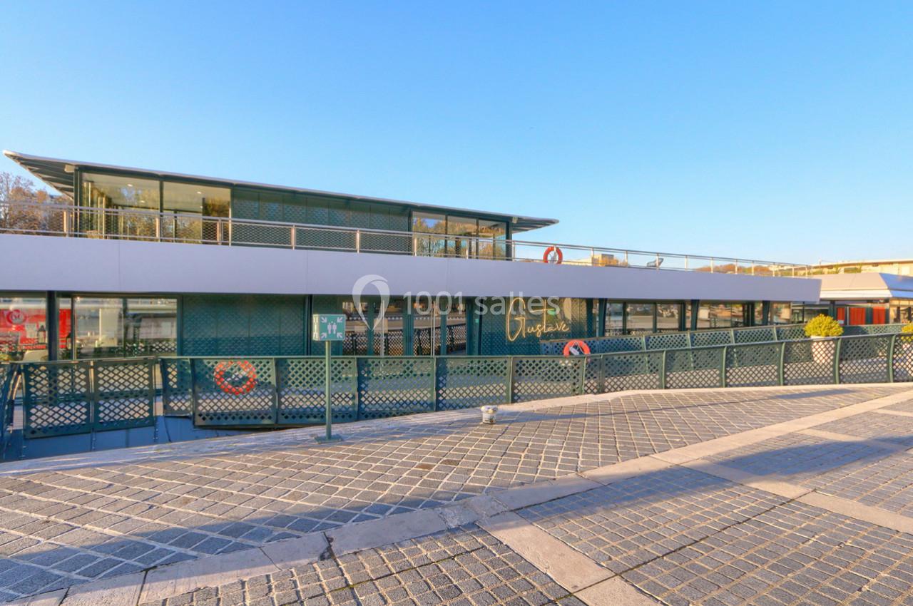 Bâtiment moderne flottant avec façade vitrée, entouré d'une passerelle et situé sur un quai pavé.