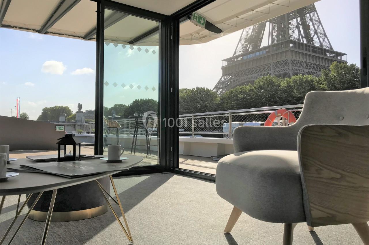 Vue intérieure d'un salon moderne avec fauteuil et table basse, donnant sur la Tour Eiffel à travers de grandes baies…