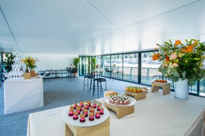 Espace intérieur lumineux avec baies vitrées donnant sur un quai, aménagé avec des fauteuils et une table basse.