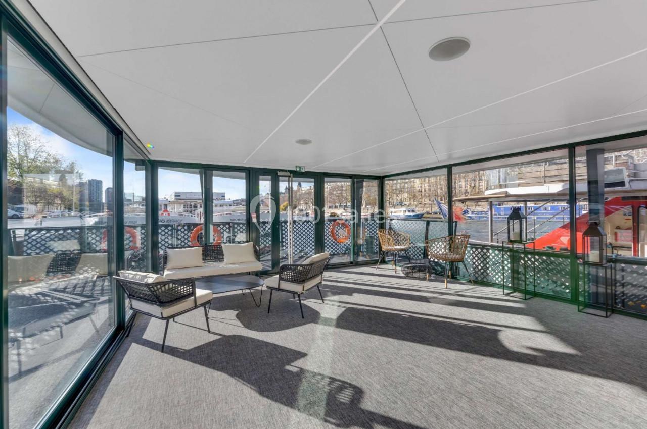 Espace intérieur lumineux avec baies vitrées donnant sur un quai, aménagé avec des fauteuils et une table basse.