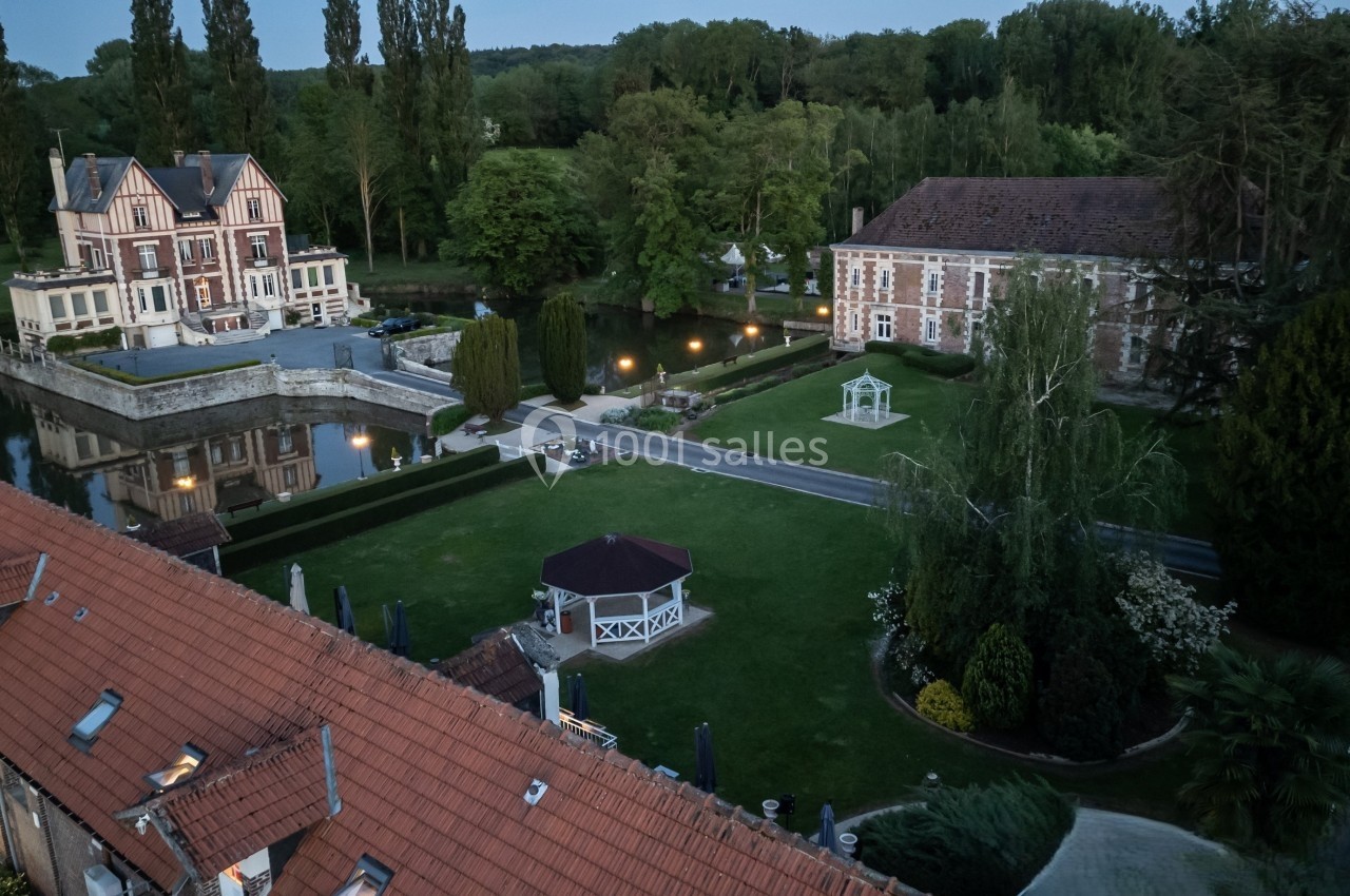 Vue aérienne d'un domaine avec un manoir, un bâtiment en briques, un parc arboré et un kiosque au centre.