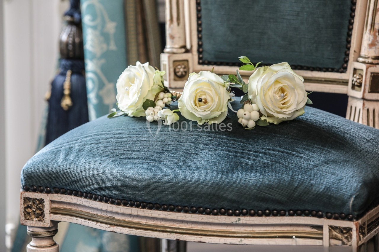 Trois roses blanches et des baies posées sur le coussin en velours bleu d'une chaise ancienne.