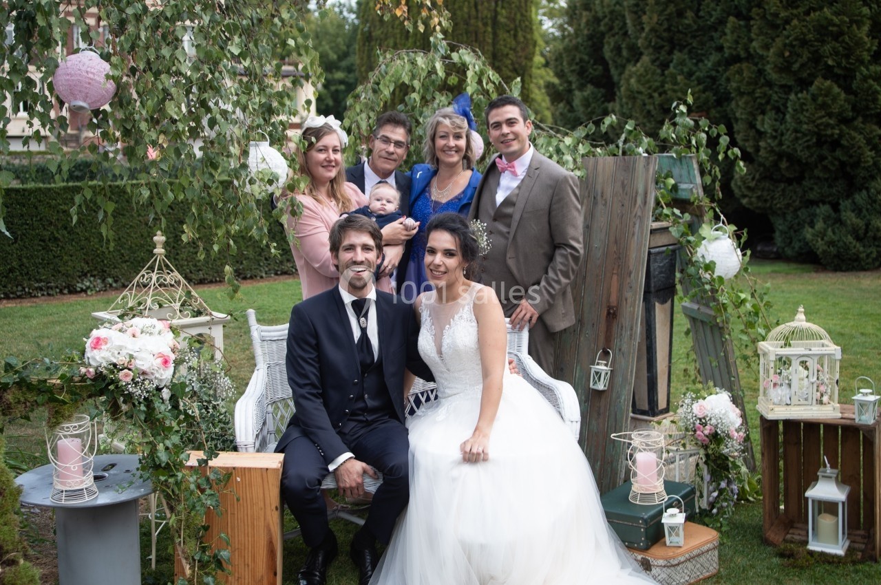 Un couple de mariés pose avec des proches dans un jardin décoré de lanternes, fleurs et éléments champêtres.