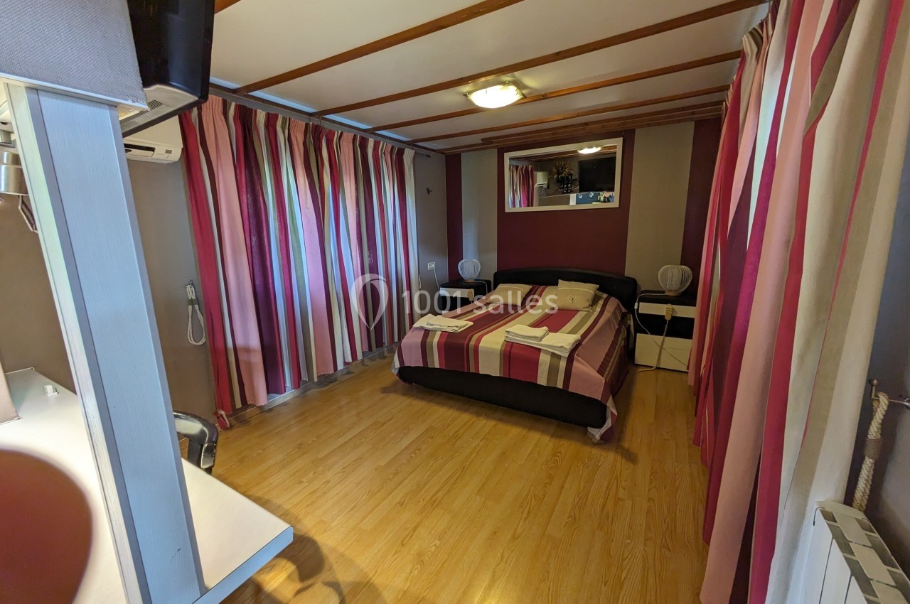 Chambre avec lit double, parquet, rideaux rayés colorés, bureau, miroir et éclairage au plafond.