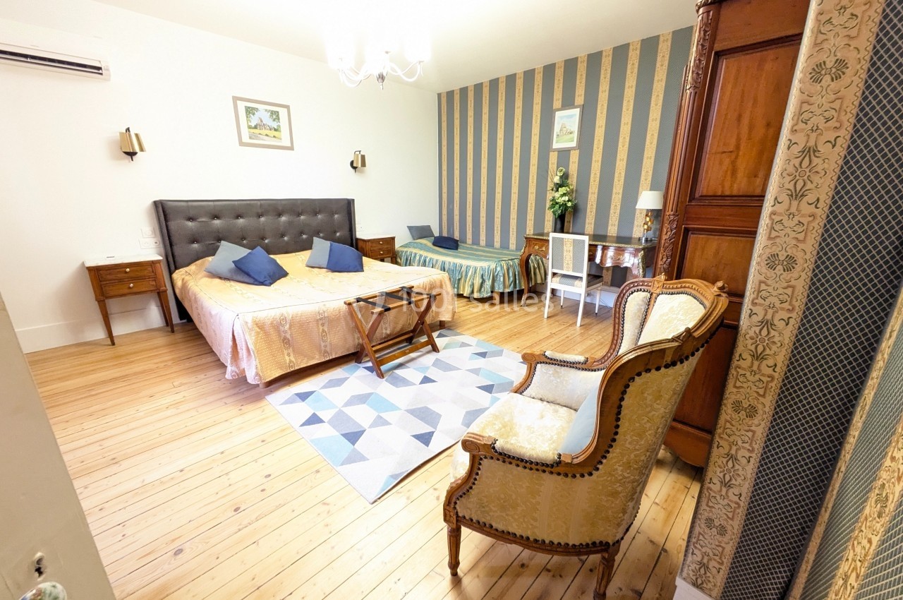 Chambre spacieuse avec lit double, lit simple, fauteuil, armoire en bois, parquet et décoration classique.