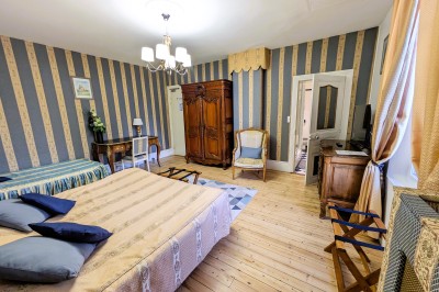 Chambre élégante avec murs bleus, lit double, cheminée, miroir doré, armoire en bois et tapis géométrique.
