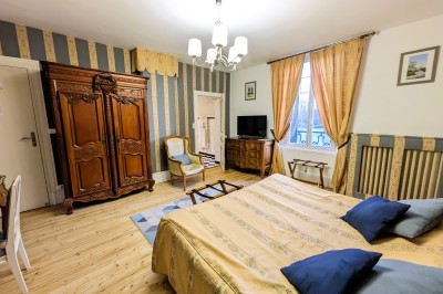 Chambre élégante avec murs bleus, lit double, cheminée, miroir doré, armoire en bois et tapis géométrique.