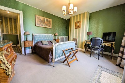 Chambre élégante avec murs bleus, lit double, cheminée, miroir doré, armoire en bois et tapis géométrique.