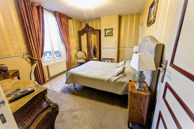 Chambre élégante avec murs bleus, lit double, cheminée, miroir doré, armoire en bois et tapis géométrique.