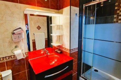 Chambre élégante avec murs bleus, lit double, cheminée, miroir doré, armoire en bois et tapis géométrique.