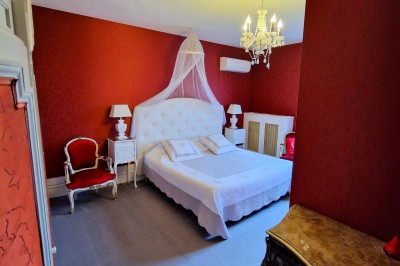 Chambre élégante avec murs bleus, lit double, cheminée, miroir doré, armoire en bois et tapis géométrique.
