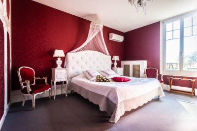 Chambre élégante avec murs bleus, lit double, cheminée, miroir doré, armoire en bois et tapis géométrique.