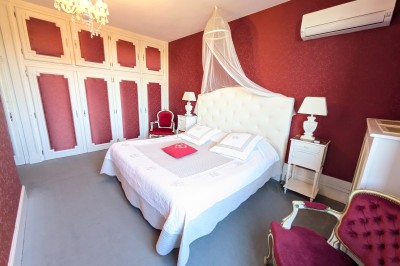 Chambre élégante avec murs bleus, lit double, cheminée, miroir doré, armoire en bois et tapis géométrique.