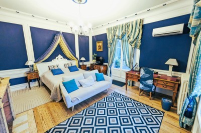 Chambre élégante avec murs bleus, lit double, cheminée, miroir doré, armoire en bois et tapis géométrique.