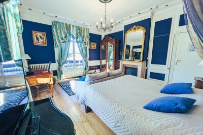Chambre élégante avec murs bleus, lit double, cheminée, miroir doré, armoire en bois et tapis géométrique.