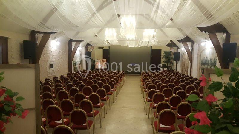 Salle de conférence avec rangées de chaises rouges alignées, plafond décoré de voilages blancs et éclairage tamisé.